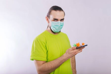 A guy in a green T-shirt is holding a smartphone with a coronavirus on the screen. Dirty phone.の写真素材