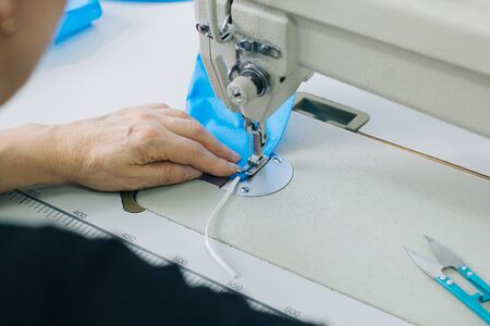 Stepwise stitching of blue fabric medical masks on a sewing machine. A close up of an industrial...