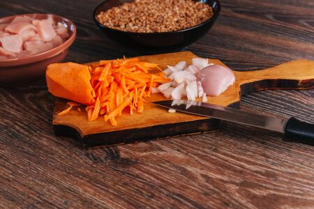 Ingredient for cooking carrots and onions on a blackboard. Uncooked diced turkey in a black cup on a dark kitchen table. Cut the fillet into pieces. Chicken meat.の写真素材