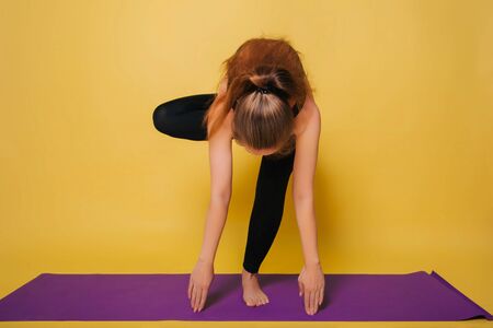 Athletic, beautiful young girl practicing yoga, doing a pose. Wear black sportswear on a plain yellow background,の写真素材