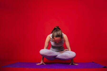 Athletic yoga, beautiful young girl practicing tolasan pose. Woman in black sportswear on a simple red backgroundの写真素材