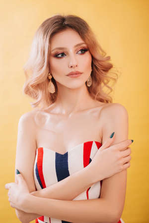 Beautiful, young model blonde close-up portrait. Girl with professional makeup and hairstyle, studio photo on a yellow background. Fashion photographyの写真素材