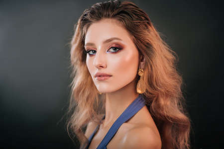 Portrait of a beautiful girl in a blue dress on a dark background. A model with professional makeup...