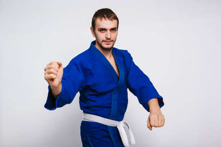 Young man in a blue kimono on a white background. The guy is a beginner in martial arts. studio photoの写真素材