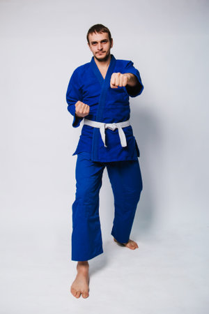 Young man in a blue kimono on a white background. The guy is a beginner in martial arts. studio photoの写真素材
