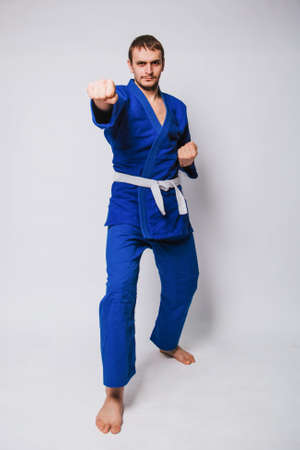 Young man in a blue kimono on a white background. The guy is a beginner in martial arts. studio photoの写真素材