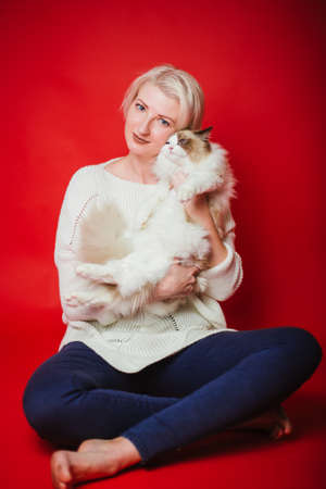 Young woman hugs a ragdoll cat on a red background. Love to the animals. Studio photoの写真素材