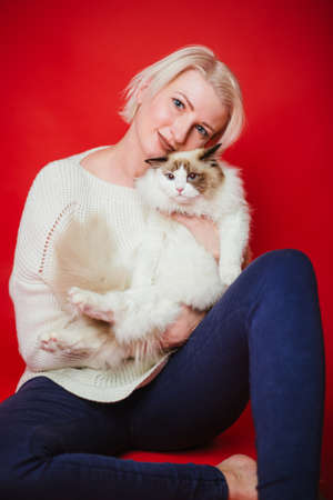 Young woman hugs a ragdoll cat on a red background. Love to the animals. Studio photoの写真素材