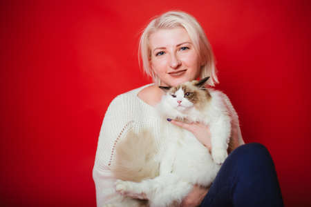 Young woman hugs a ragdoll cat on a red background. Love to the animals. Studio photoの写真素材