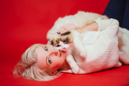 Young woman hugs a ragdoll cat on a red background. Love to the animals. Studio photoの写真素材