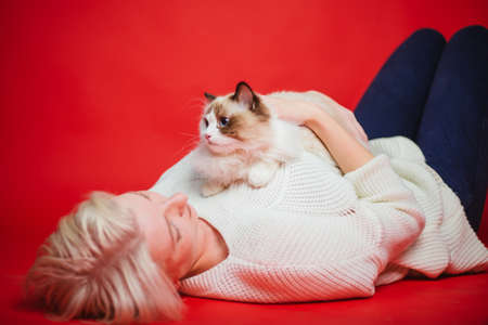 Young woman hugs a ragdoll cat on a red background. Love to the animals. Studio photoの写真素材