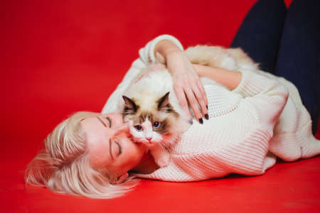 Young woman hugs a ragdoll cat on a red background. Love to the animals. Studio photoの写真素材