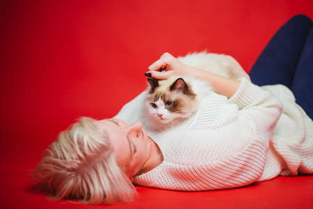 Young woman hugs a ragdoll cat on a red background. Love to the animals. Studio photoの写真素材