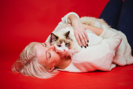 Young woman hugs a ragdoll cat on a red background. Love to the animals. Studio photoの写真素材