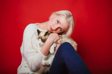 Young woman hugs a ragdoll cat on a red background. Love to the animals. Studio photoの写真素材