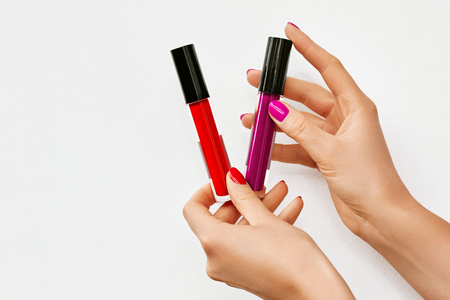 Female hands with lip glosses isolated on white. Woman holding Red and Pink lip glosses. Space for textの写真素材
