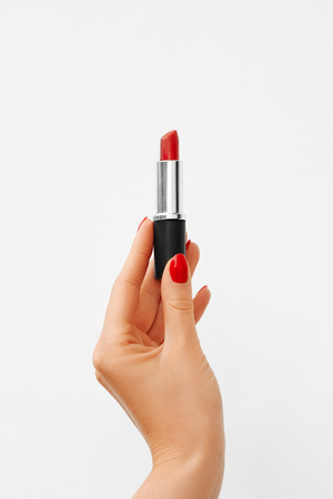 The hand with red manicure holds a bright red lipstick on white backgroundの写真素材
