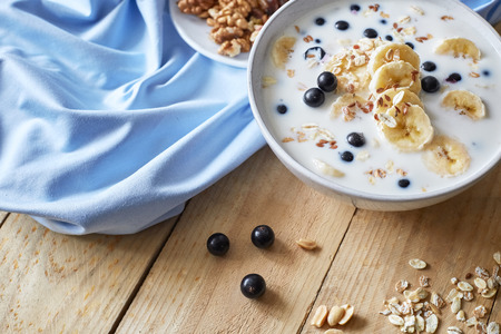Oatmeal porridgewith bananas, nuts, raisins, blueberries and milk on table on wooden  background.  Healthy breakfast and diet food.の写真素材