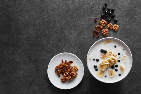 Healthy breakfast concept with oatmeal porridge with bananas, milk, blueberries,  nuts, raisins, chia seeds and currants. Top view. Super foodの写真素材