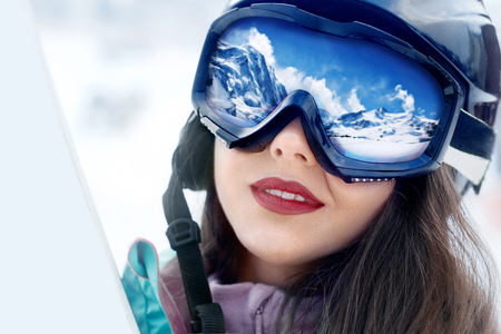 Portrait of young woman at the ski resort on the background of mountains and blue sky.A mountain range reflected in the ski maskの写真素材
