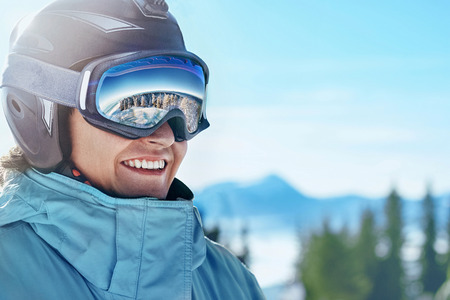 Close up of the ski goggles of a man with the reflection of snowed mountains.  A mountain range reflected in the ski mask.  Portrait of man at the ski resort on the background of mountains and skyの写真素材