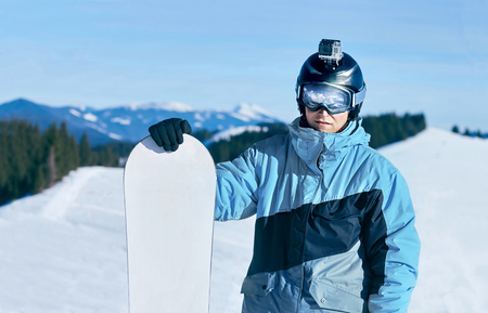 Men snowboarder stands with snowboard on mountain backdrop.の写真素材