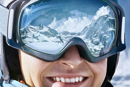 Portrait of man at the ski resort on the background of mountains and blue sky.A mountain range reflected in the ski maskの写真素材