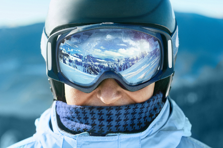 Close up of the ski goggles of a man with the reflection of snowed mountains.  A mountain range reflected in the ski mask.  Portrait of man at the ski resort on the background of mountains and skyの写真素材