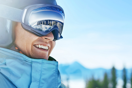 Close up of the ski goggles of a man with the reflection of snowed mountains.  A mountain range reflected in the ski mask.  Portrait of man at the ski resort on the background of mountains and skyの写真素材