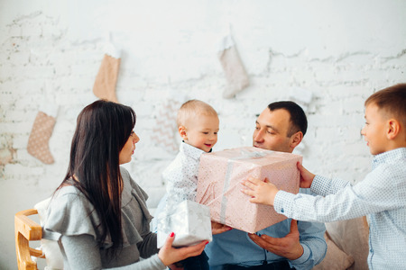 Happy Young Family With Two Children Holding Christmas Gift and Smiling at Camera Near Christmas tree. New Year Celebration. Decorations.  Xmas eventの写真素材