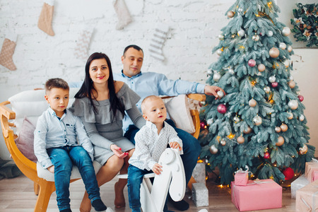 Happy Young Family With Two Children is waiting Christmas t and Smiling at Camera Near Christmas tree. New Year Celebration. Decorations.  Xmas eventの写真素材