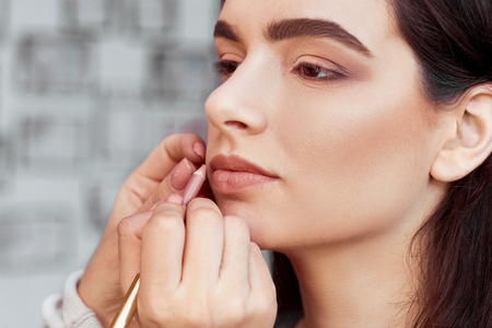 Process of making makeup. Make-up artist working with brush on model face. Portrait of young  woman in beauty saloon interior. Applying tone to skin.の写真素材