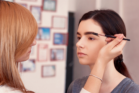 Process of making makeup. Make-up artist working with brush on model face. Portrait of young  woman in beauty saloon interior. Applying tone to skin.の写真素材