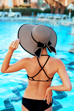 Elegant sexy woman in the bikini on the sun-tanned slim and shapely body is posing near the swimming pool.  Girl with sun hat relaxing in resort spa hotel on travel holidays vacation.の写真素材