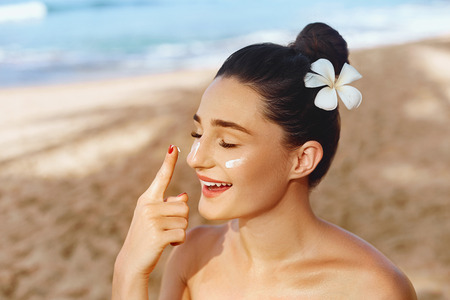 Beautiful  Woman smile applying sun cream on face. Skincare. Body Sun protection. sunscreen. Female in hat smear moisturizing lotion on skinの写真素材