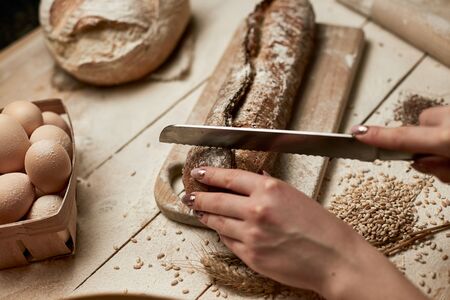 Whole grain bread put on kitchen wood plate with a chef holding gold knife for cut. Fresh bread on table close-up. Fresh bread on the kitchen tableの写真素材