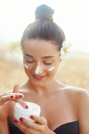 Face Skincare. Beauty and Spa Concept. Portrait of female holding moisturizing cream in her hand. Young pretty woman applying cosmetic cream. Soft skin model with light nude make-up.の写真素材