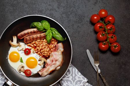 English breakfast in cooking pan with fried eggs, sausages,beans, tomatoes, mushrooms, bacon and toast on wooden background.  Copy space. Top viewの写真素材