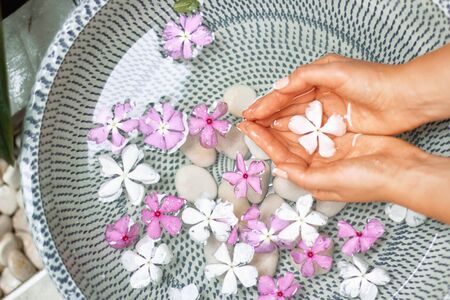 Hands of Young girl with natural manicure on fingernails and bowl with water and flower.Spa treatment and massage for female hands.Close up.Spa skin and body nails careの写真素材