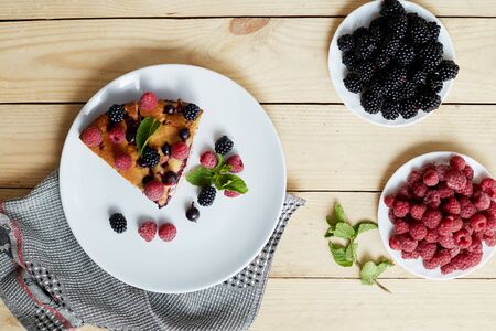 Piece of pie with blueberries, rasberry and mint for dessert on a white plate, napkin. Pieces of delicious homemade cake on a wooden boards backgroundの写真素材
