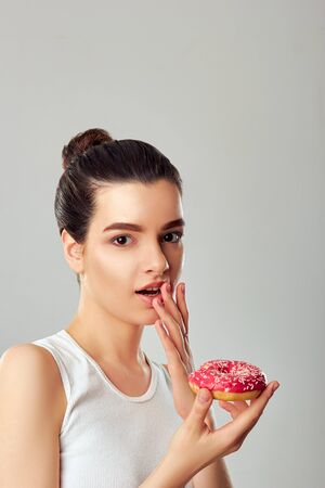 Young Woman Eating Donut. Brunette Girl Tastes a Donut. Sweets Are Unhealthy Junk Food. Dieting, Healthy Eating, Lifestyle. Weight Lossの写真素材