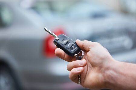 Business man hand holding car keys front with car on background. parking in front of the house....