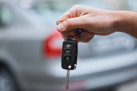 Close up hand of Man holding car key  with blurred car on background.