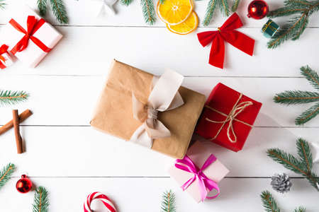 Beautiful Christmas composition on wooden white background with Christmas gift boxes, snowy fir branches, conifer cones, cinnamon dried fruits, holiday decoration, caramel stick. New Year. Top view, copy space.の写真素材
