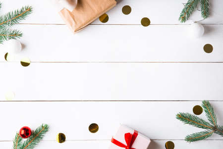 Beautiful Christmas composition on wooden white background with Christmas gift boxes, snowy fir branches, conifer cones, cinnamon dried fruits, holiday decoration, caramel stick. New Year. Top view, copy space.