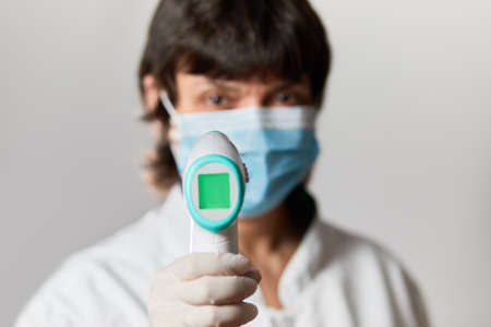 Doctor wearing protective mask ready to use infrared forehead thermometer to check body temperature for virus symptoms - epidemic virus outbreak concept. Coronavirus.Thermometer gunの写真素材