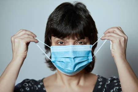 Portrait of young woman wearing a face mask, looking at camera, close up, isolated on gray...