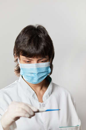 Doctor looking at thermometer. Female hands holding a digital thermometer. Girl measures the temperature. Check body temperature for virus symptoms flu, epidemic coronavirusの写真素材