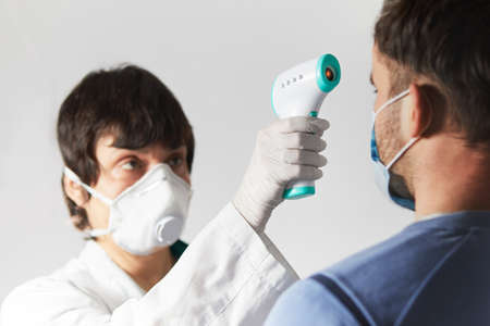 Doctor wearing a respirator N95 mask to use infrared forehead thermometer to check body temperature for virus symptoms. Respiratory diseases such as flu, coronavirus. Epidemic outbreakの写真素材