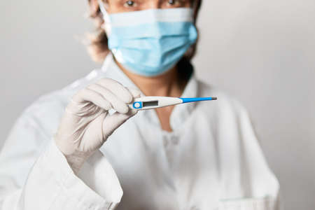 Doctor looking at thermometer. Female hands holding a digital thermometer. Girl measures the temperature. Check body temperature for virus symptoms flu, epidemic coronavirusの写真素材